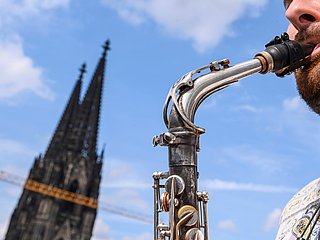 Spitze des Kölner Doms und ein Ausschnitt eines Saxofonspieler*in