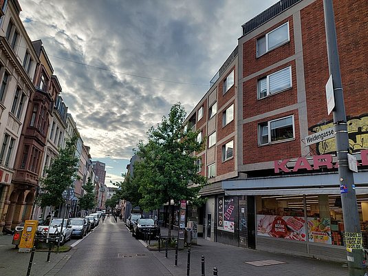 Bick in eine Straße mit parkenden Autos, einem Geschäft und einer Person auf dem Fahrrad